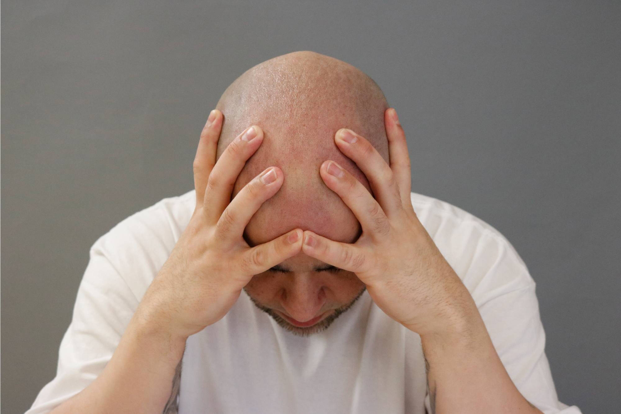 Photograph of a man looking down with his head in his hands.